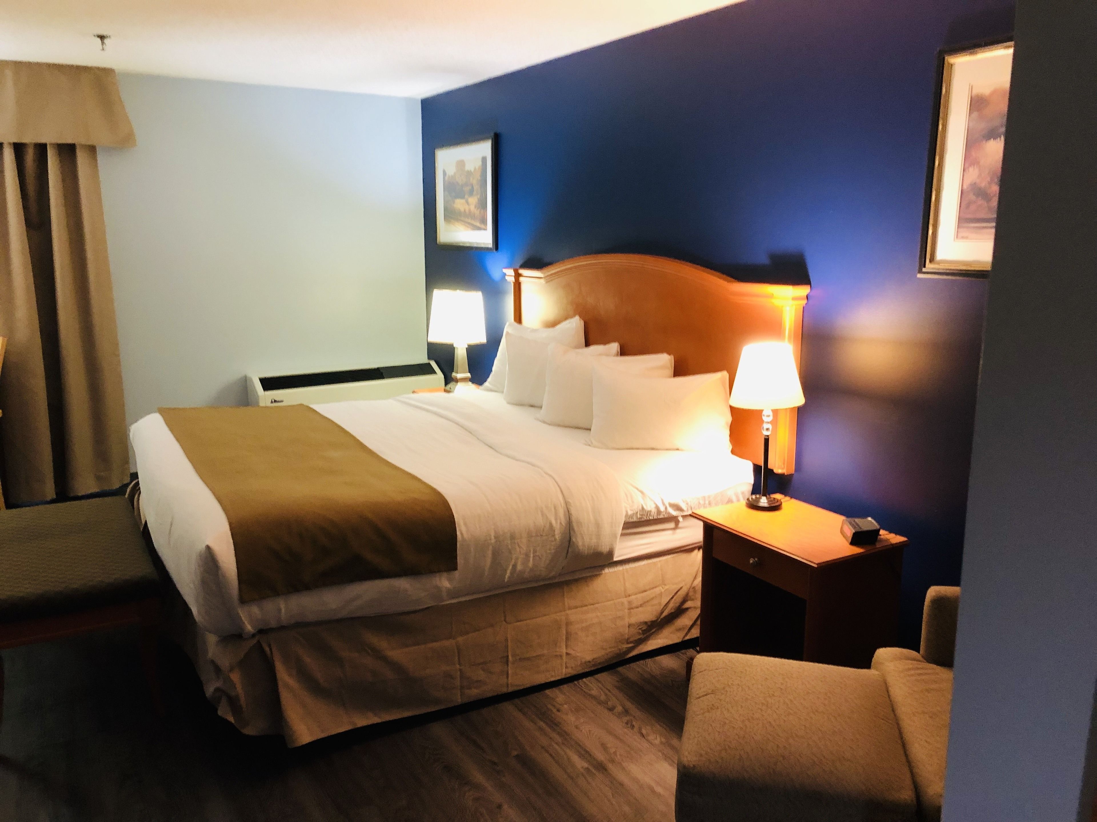 A hotel room with a large bed, two bedside lamps, a wooden headboard, and a framed picture on the wall.