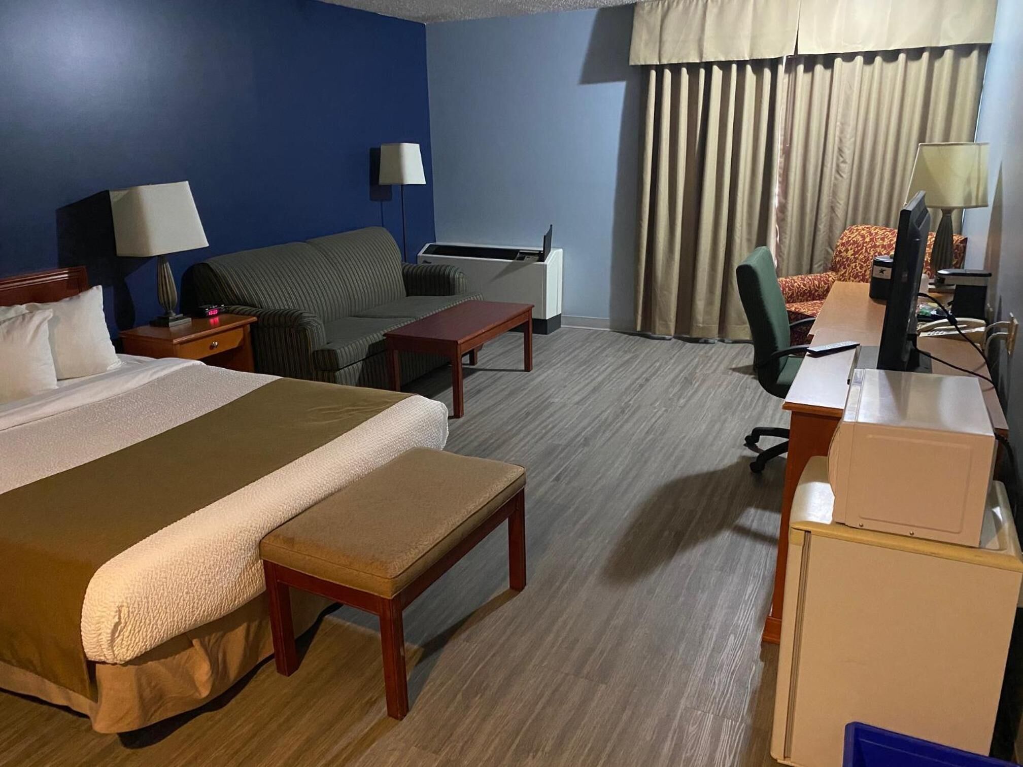 Ett hotellrum med en stor säng, ett skrivbord, en stol, en soffa och en tv.