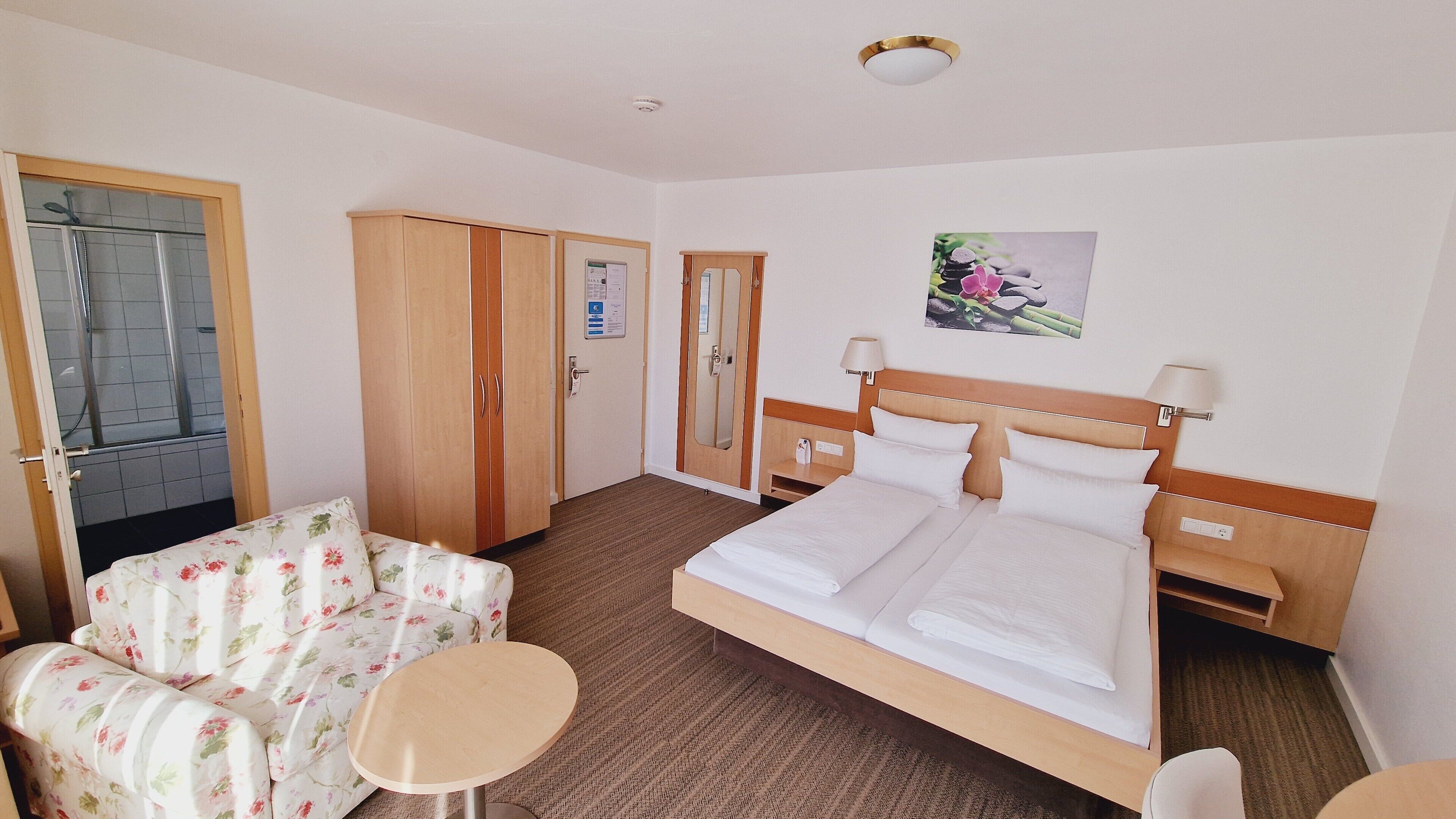 Une chambre d’hôtel avec un lit, un canapé à motifs floraux, une petite table et une armoire.