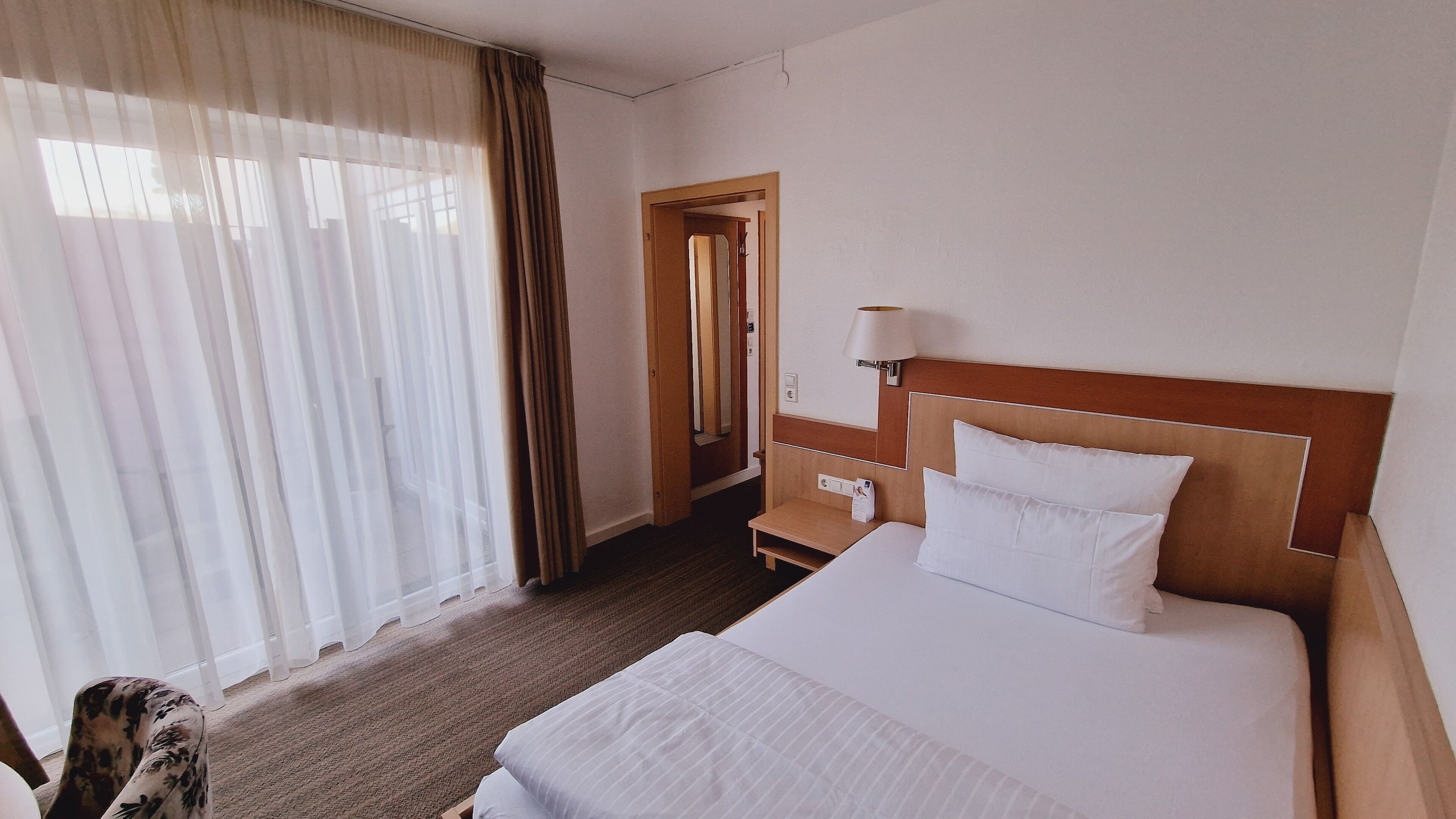 A hotel room with a bed, a nightstand, a lamp, and a mirror.