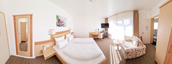 A hotel room with a bed, a desk, a TV, a sofa, and a bathroom visible through an open door. - Hotel Garni Superior (Metzingen)
