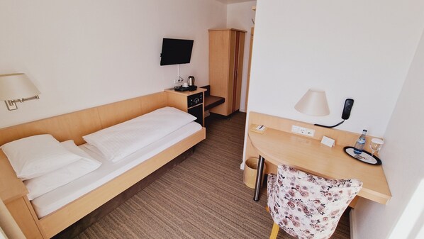 Une chambre d’hôtel avec un lit, un bureau doté d’une lampe, un téléphone et un téléviseur fixé au mur.