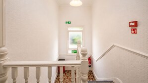 A staircase with white balusters, a fire extinguisher, and an exit sign. - Saji Hotel Ilford (Ilford)