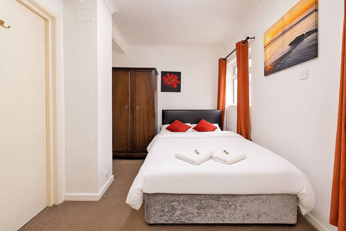A hotel room with a bed, a wooden wardrobe, a painting on the wall, and a door.