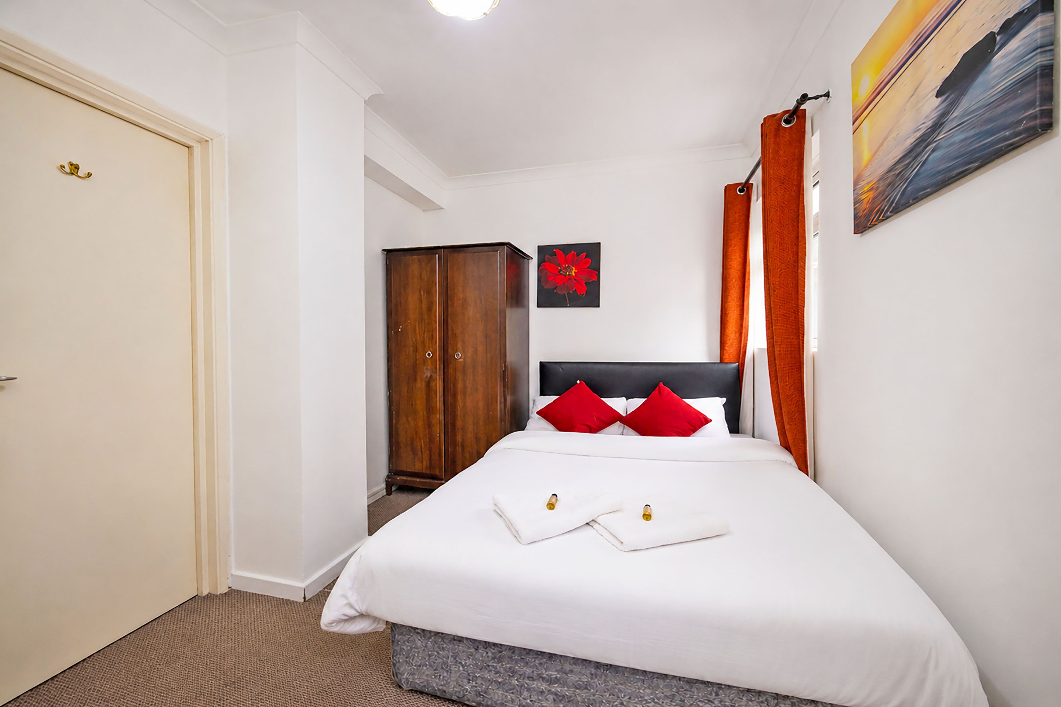 A hotel room with a bed, a wardrobe, a painting, and a door.
