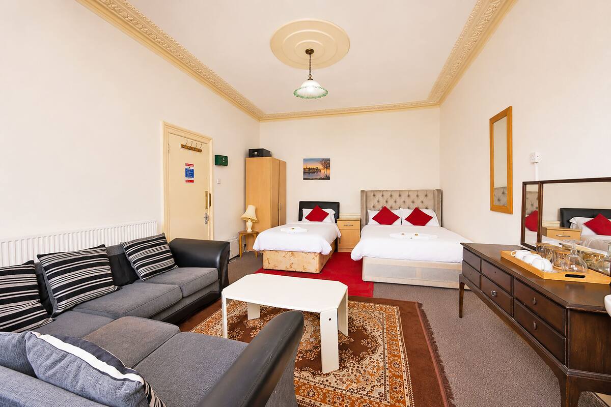 A hotel room with a sofa, two beds, a dresser, a mirror, and a ceiling light.