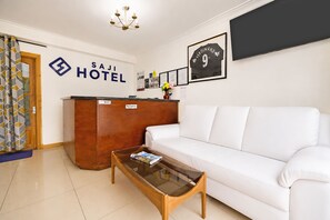 A hotel reception area with a reception desk, a white sofa, a glass coffee table, and a framed jersey on the wall.