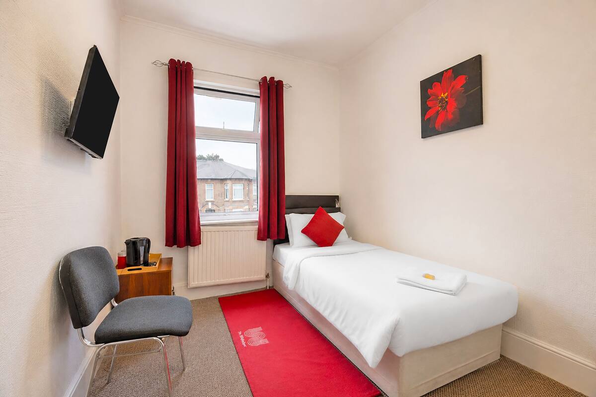 A hotel room with a bed, a chair, a TV, a window with curtains, and a painting on the wall.