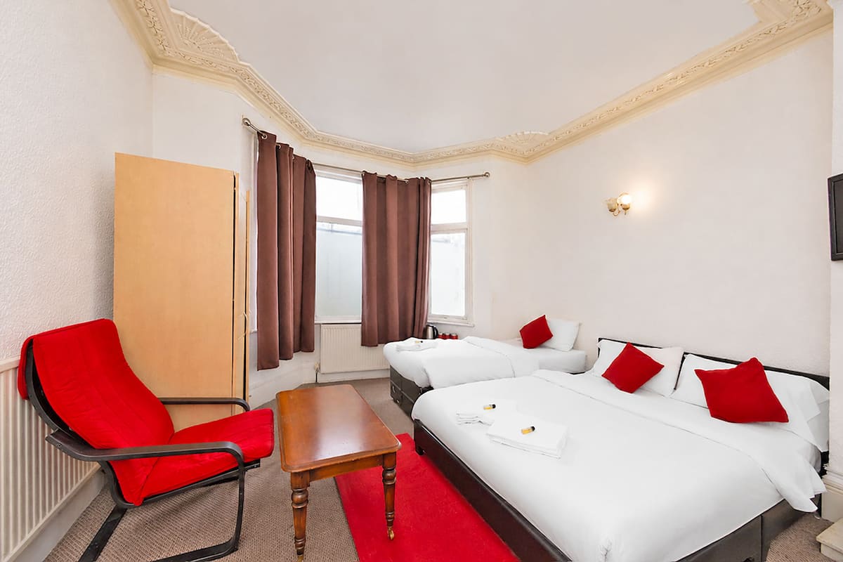 A hotel room with a bed, two bedside tables, a chair, a wardrobe, and a window with curtains.