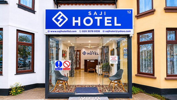 A hotel entrance with a clear sign, a reception desk, and two chairs outside. - Saji Hotel Ilford (Ilford)