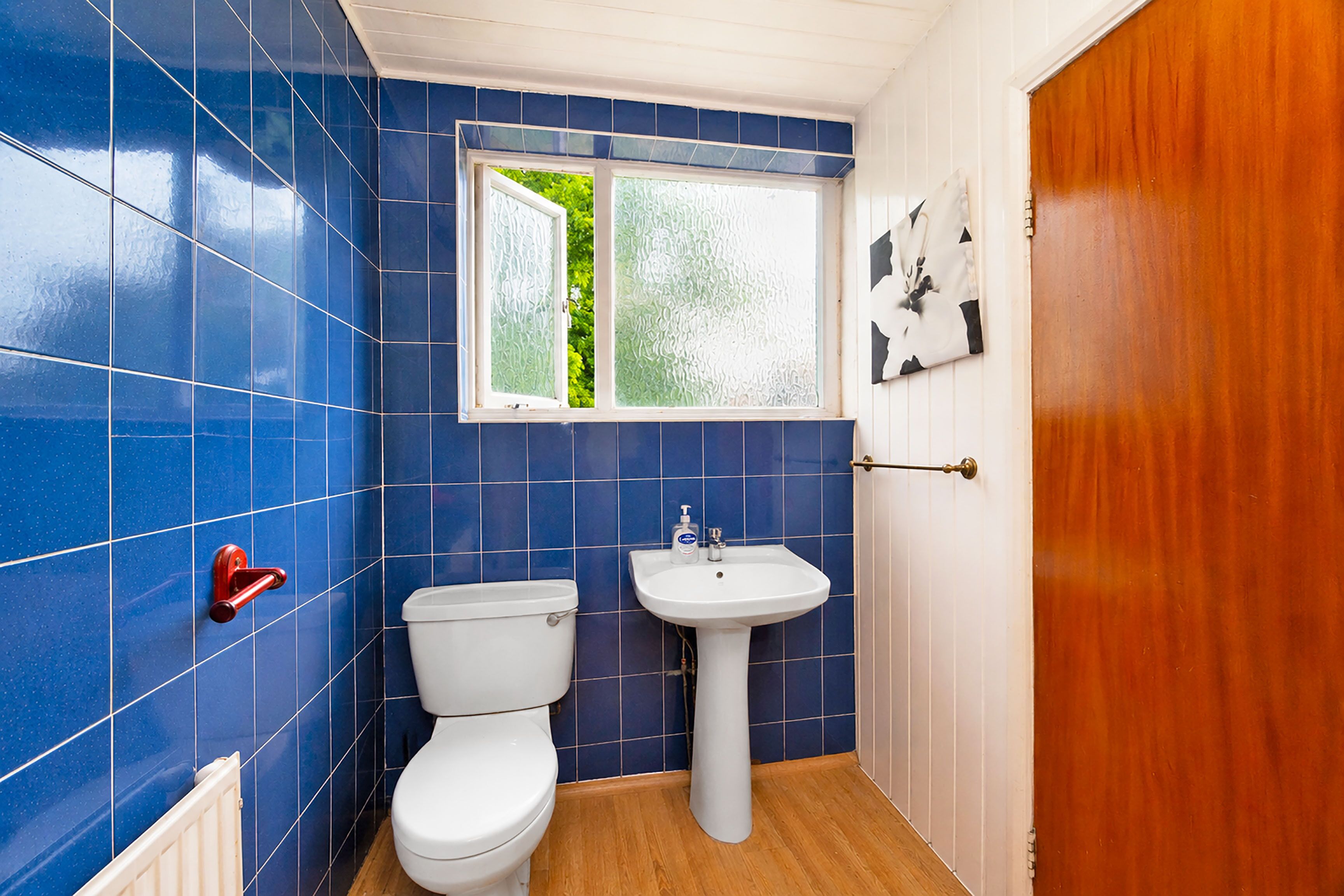 Un baño con azulejos azules, un inodoro blanco, un lavamanos blanco y una puerta de madera.