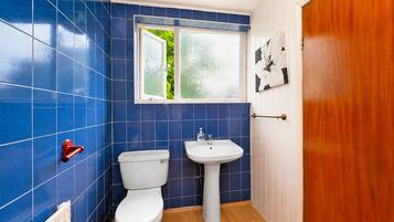 Un baño con azulejos azules, un inodoro blanco, un lavamanos blanco y una puerta de madera.