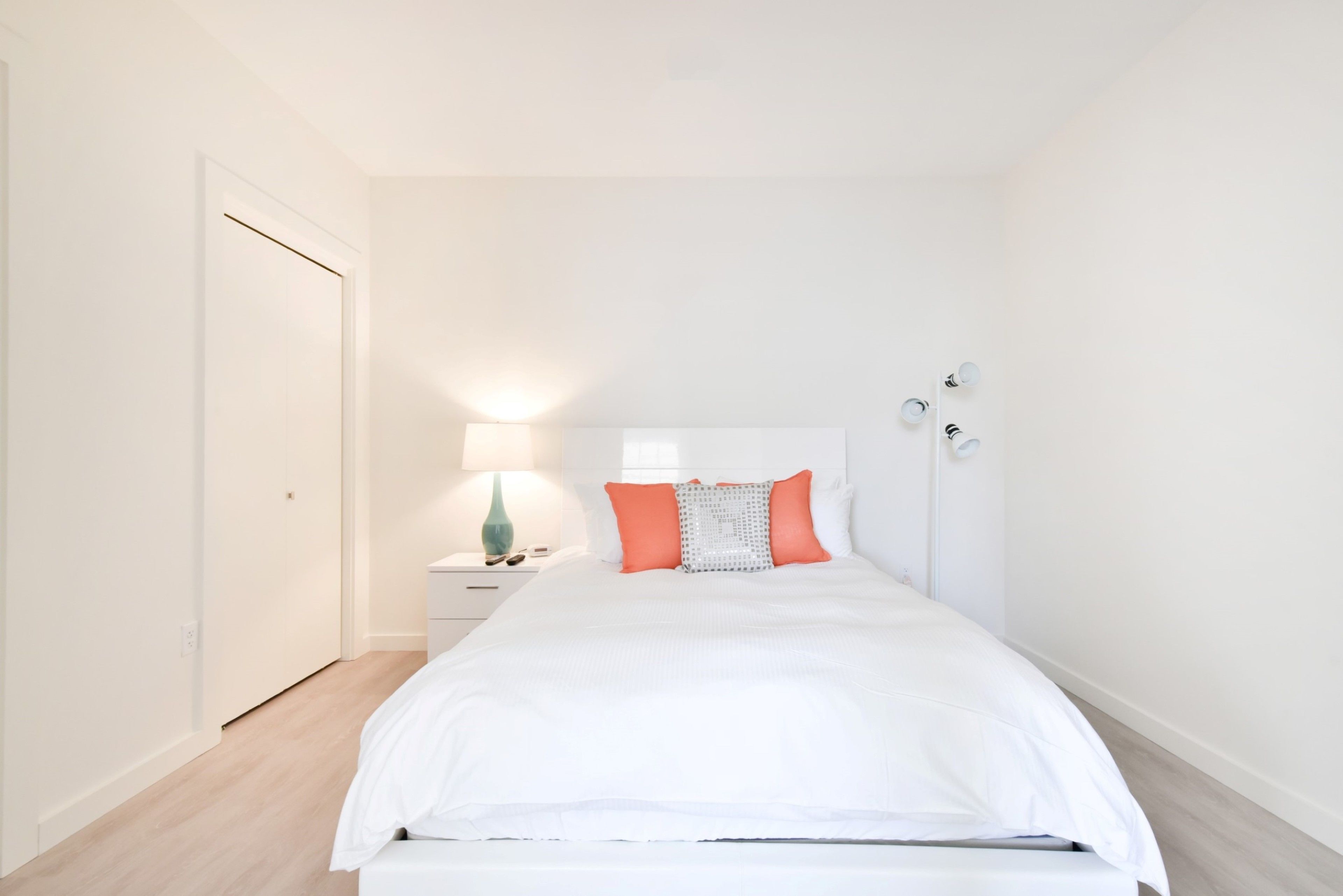 A bedroom with a bed, a nightstand, a lamp, and a door.