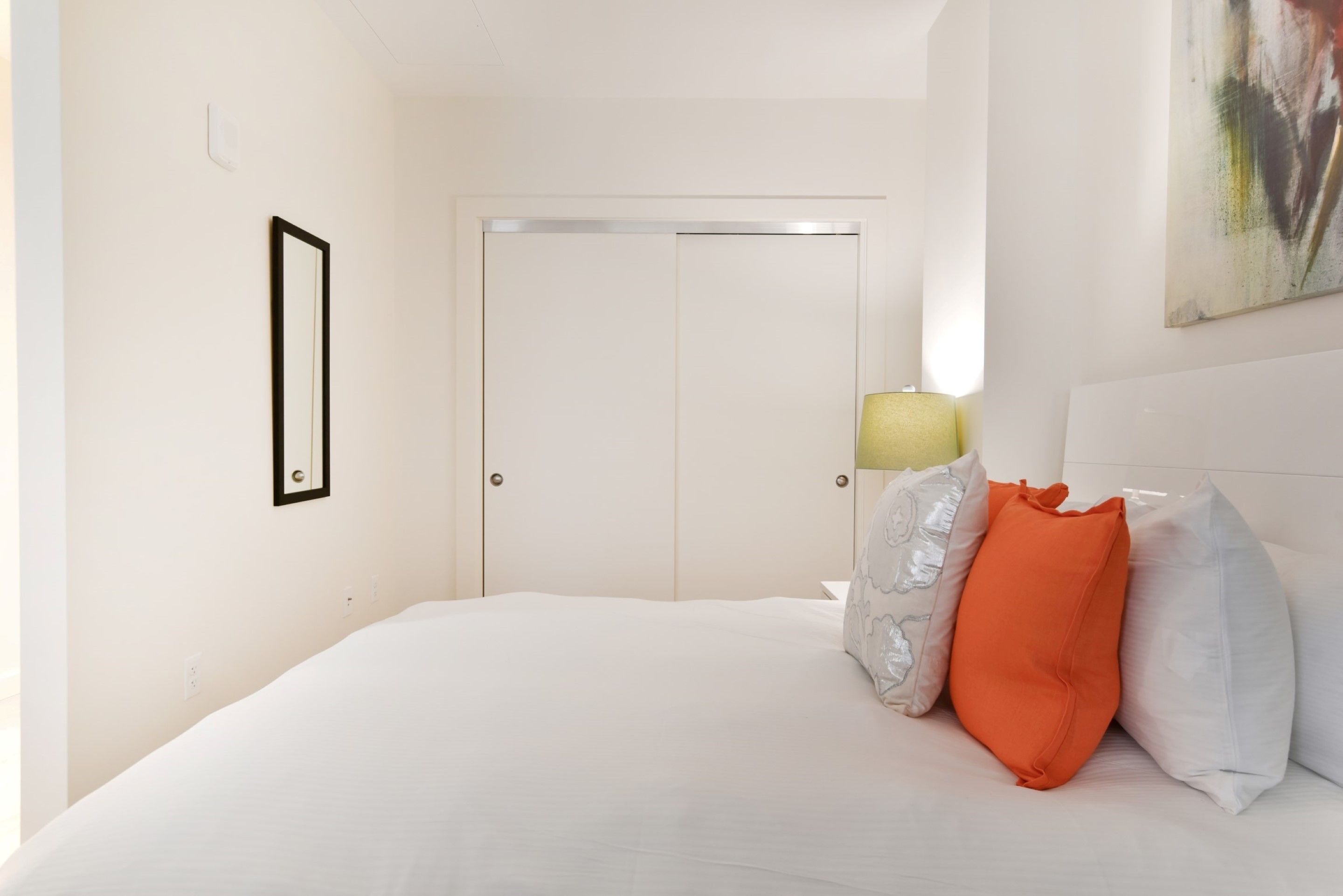 Une chambre à coucher avec un lit, des oreillers, une porte et un tableau accroché au mur.