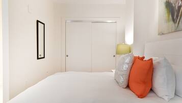Een slaapkamer met een bed, kussens, een deur en een aan de muur hangend schilderij.