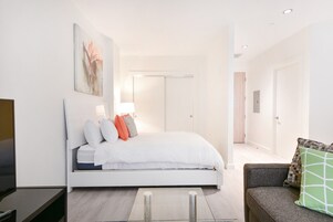 Ein modernes Schlafzimmer mit Bett, Fernseher, Sofa und einem zur Tür führenden Flur.