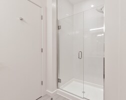 Un baño moderno con cabina de ducha de vidrio, una puerta blanca y suelo de baldosas.