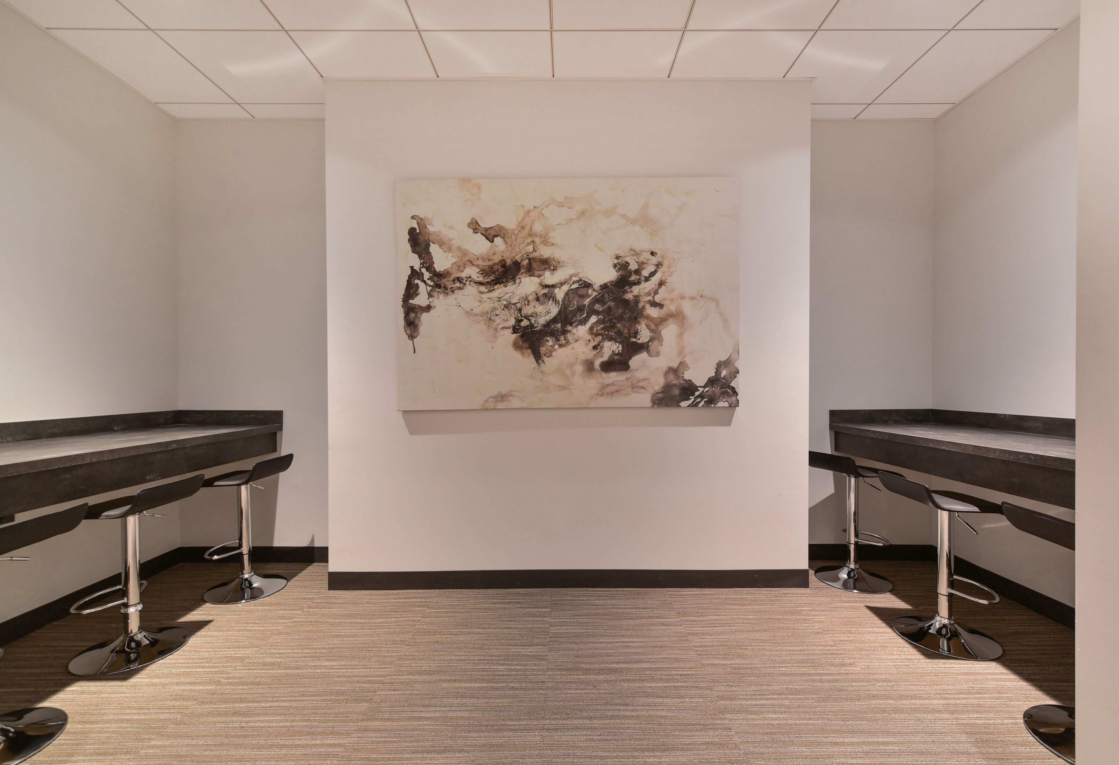 A modern bar area with two bar stools and a large abstract painting on the wall.