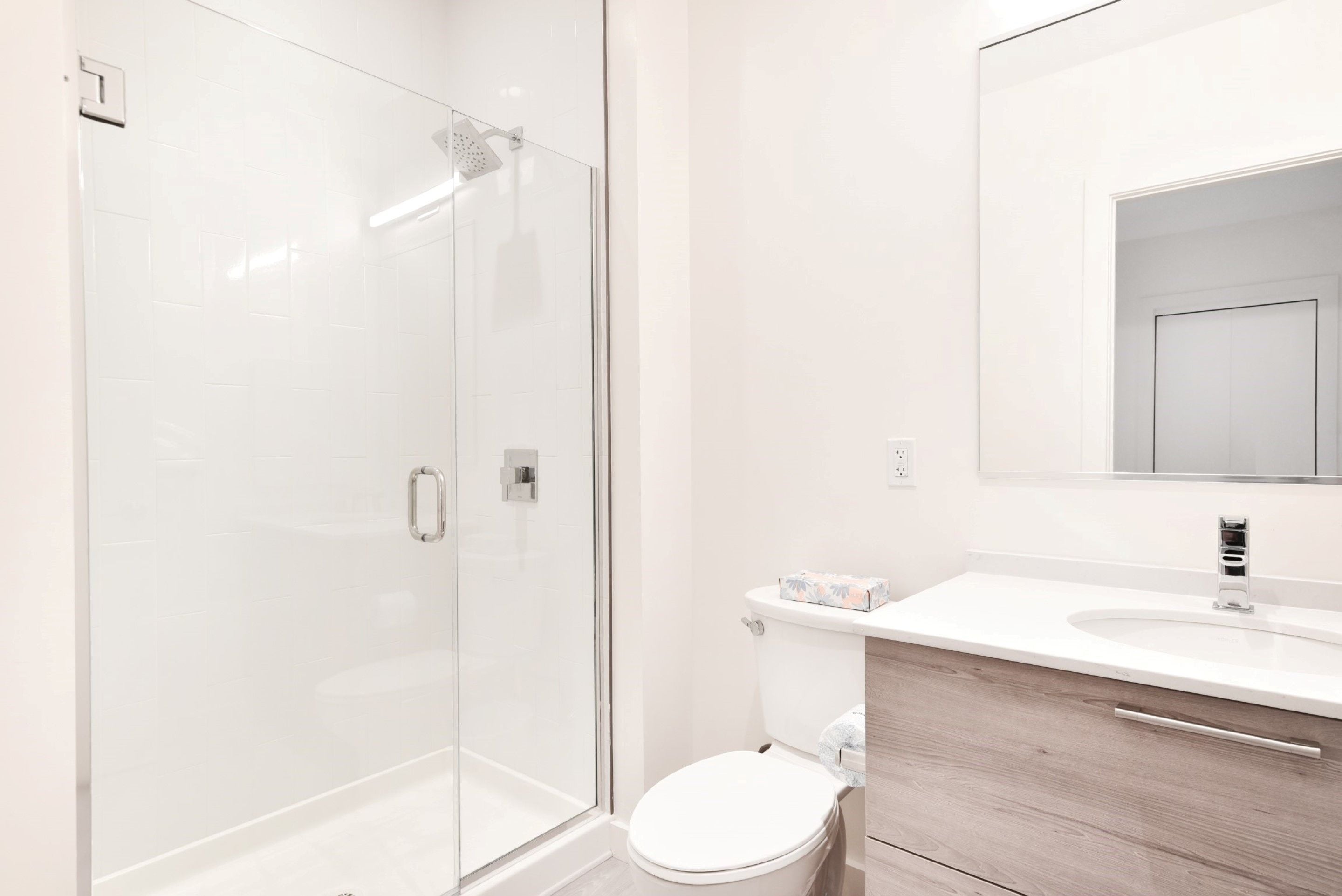 Un baño moderno con cabina de ducha de vidrio, inodoro blanco y tocador de madera con espejo.