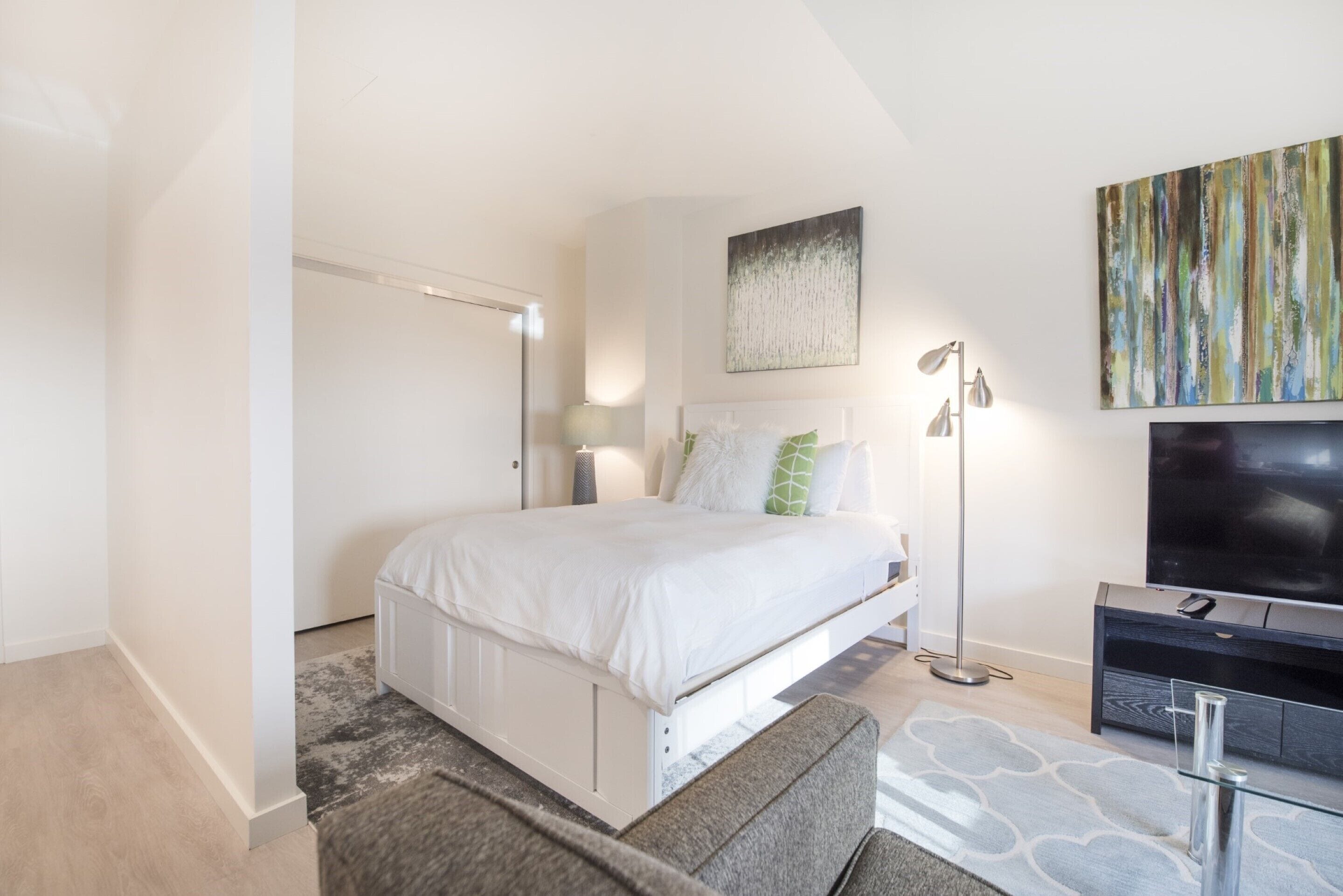 Una camera da letto moderna con un letto, un comodino, una lampada, una TV e opere d'arte.