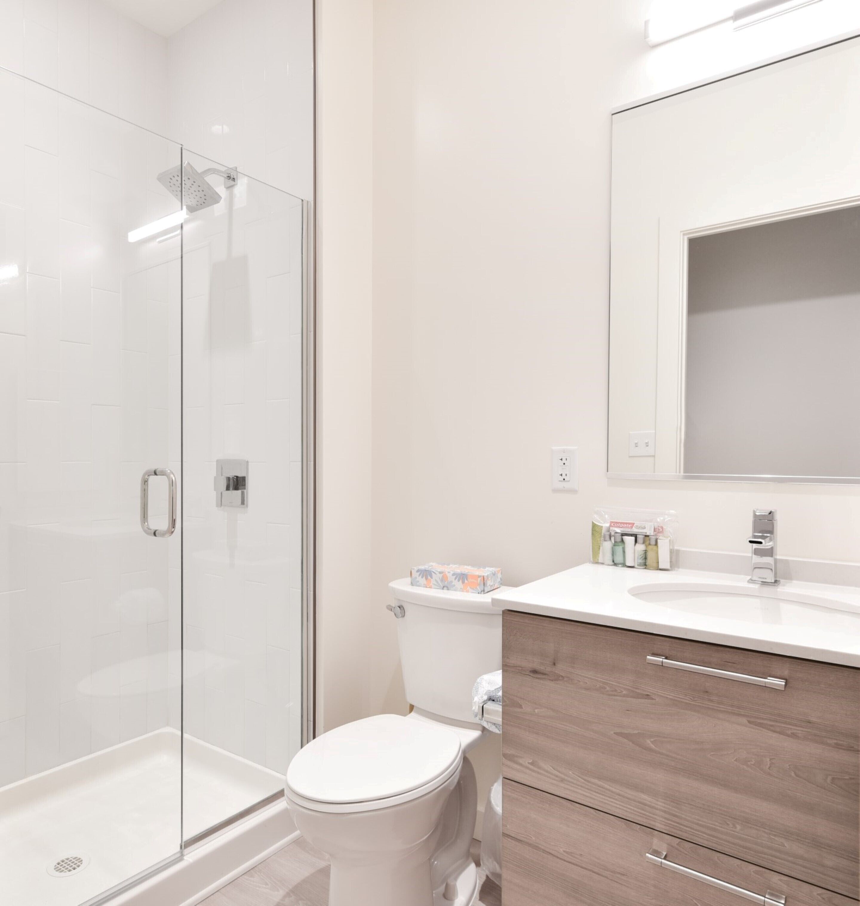 Un baño moderno con cabina de ducha de vidrio, inodoro y tocador con espejo.