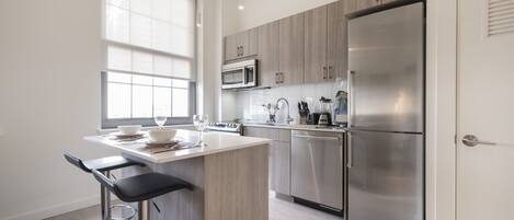 Eine moderne Küche mit einer zentralen Kochinsel, Edelstahlgeräten und einem Fenster, das für natürliches Licht sorgt.