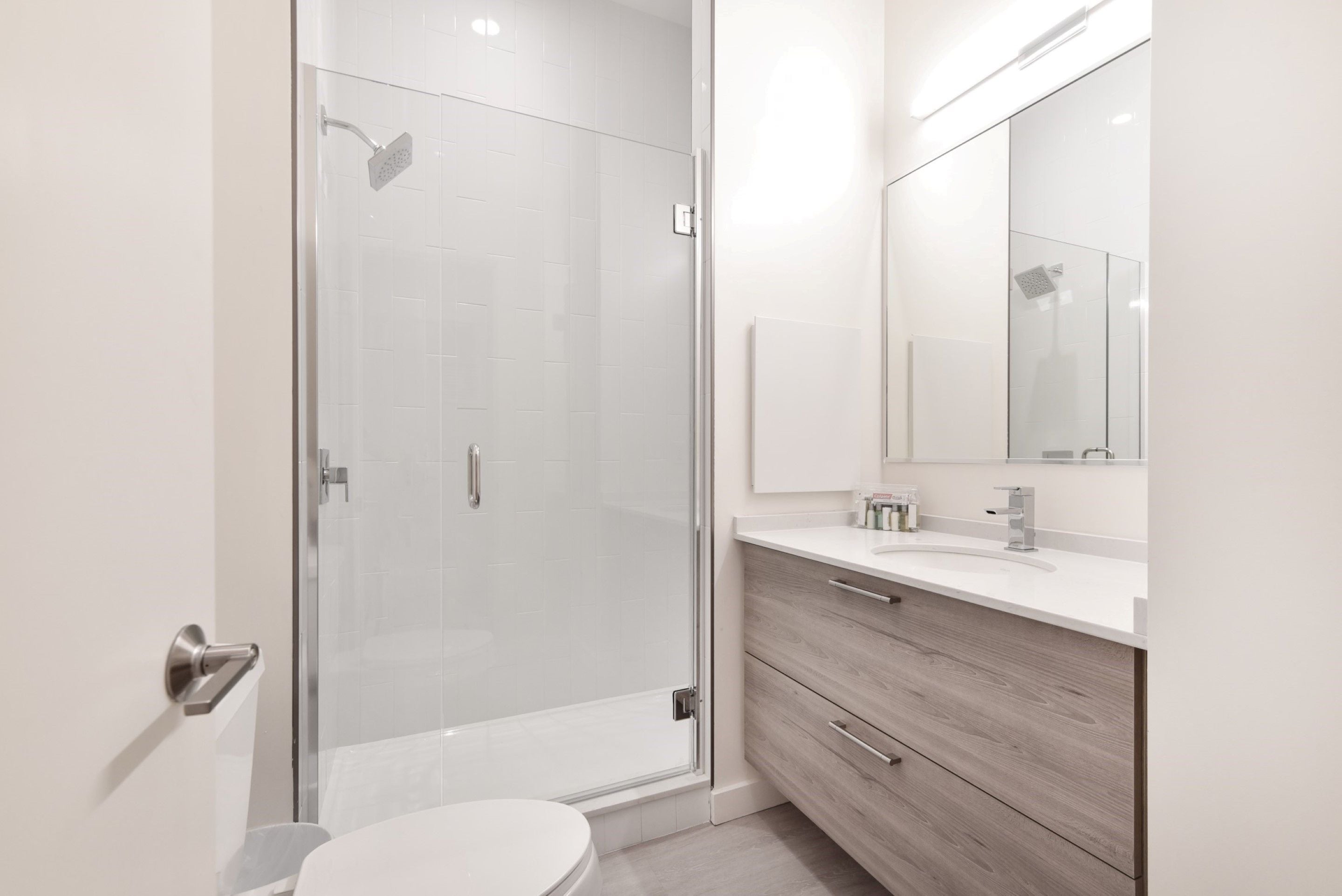 A modern bathroom with a glass shower enclosure, a white toilet, and a vanity with a mirror and drawers.