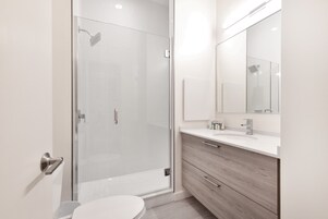 Een moderne badkamer met een glazen douchecabine, een wit toilet en een wastafel met een spiegel en lades.