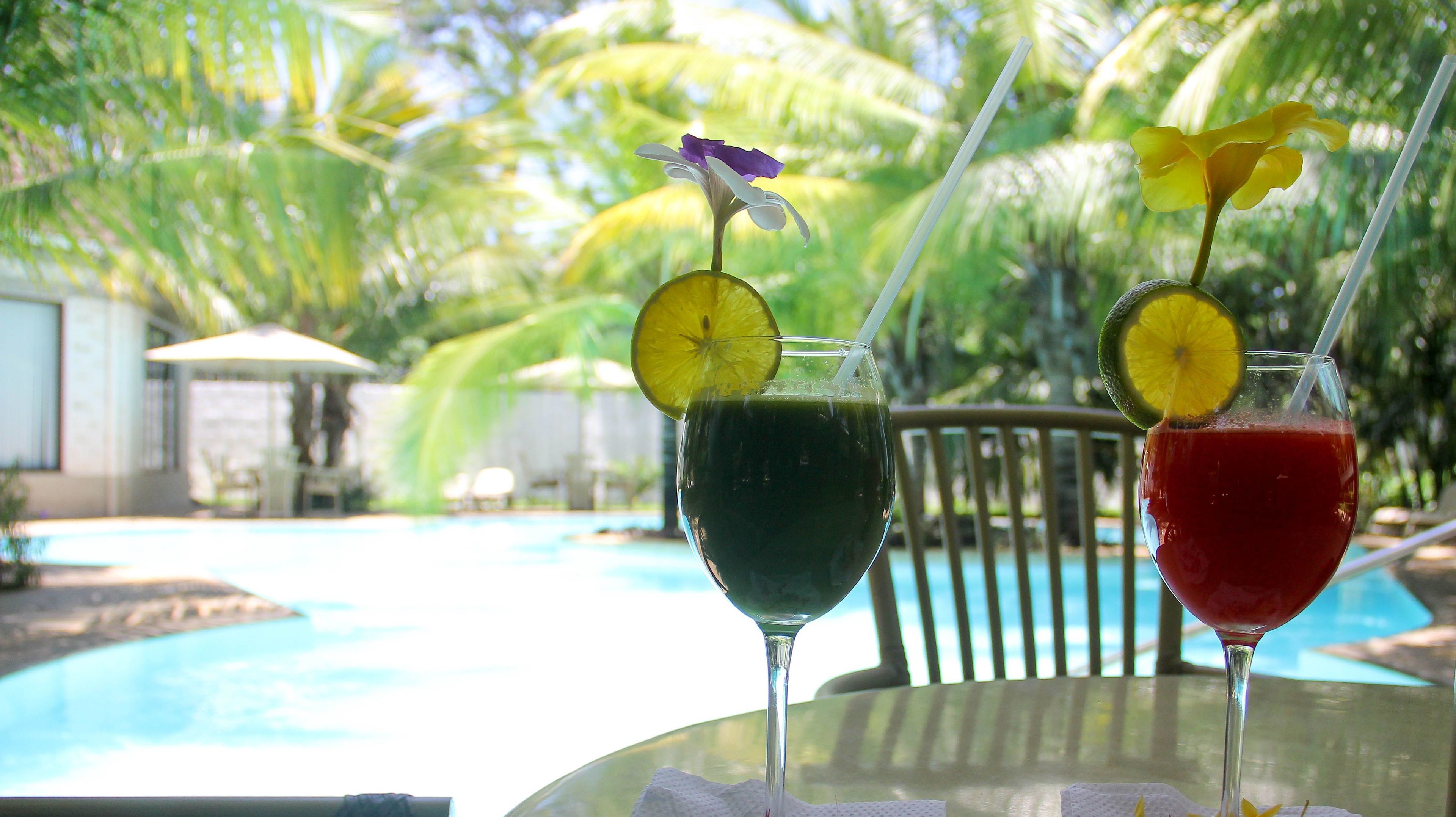 Two drinks with fruit garnishes on a table by a poolside.