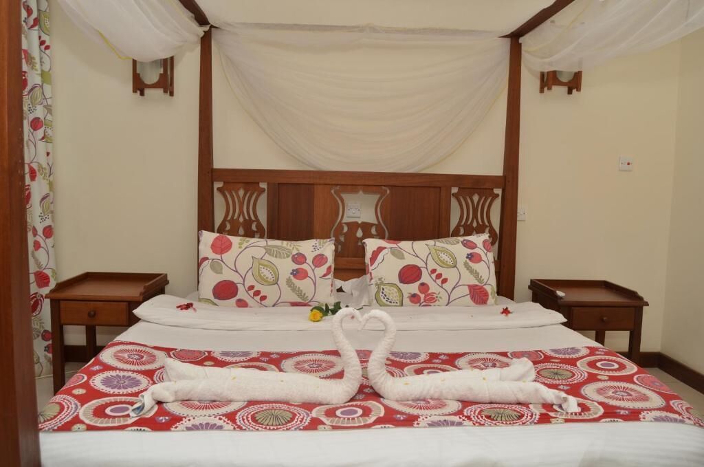 A bed with a canopy, floral-patterned pillows, and two swan-shaped towels.