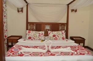 Uma cama com dossel, almofadas estampadas com flores e duas toalhas em formato de cisne.