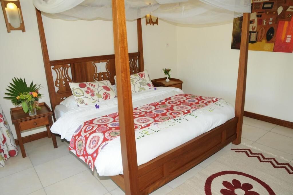 Una cama con dosel con cubrecama floral, una mesita de noche con un florero y un espejo montado en la pared.