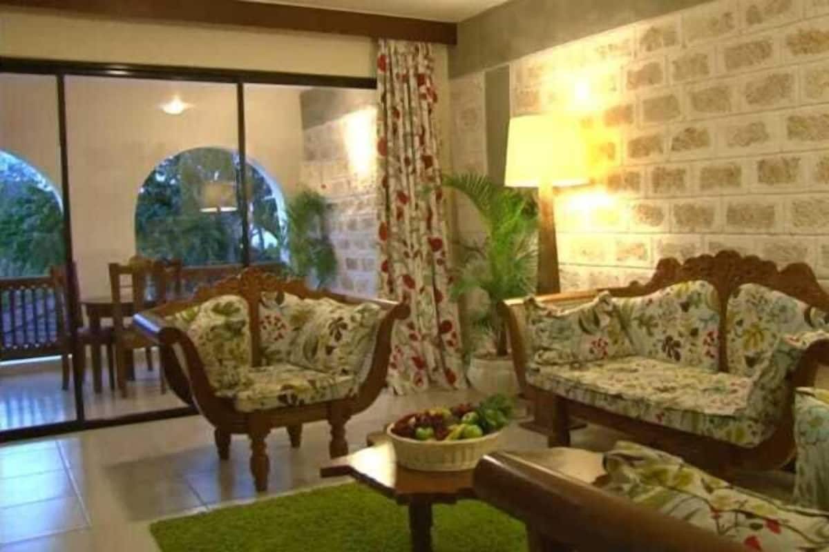 Ein Zimmer mit zwei Sofas mit Blumenmuster, einem Couchtisch mit Obstschale und einem großen Fenster mit Blick auf Grünflächen.