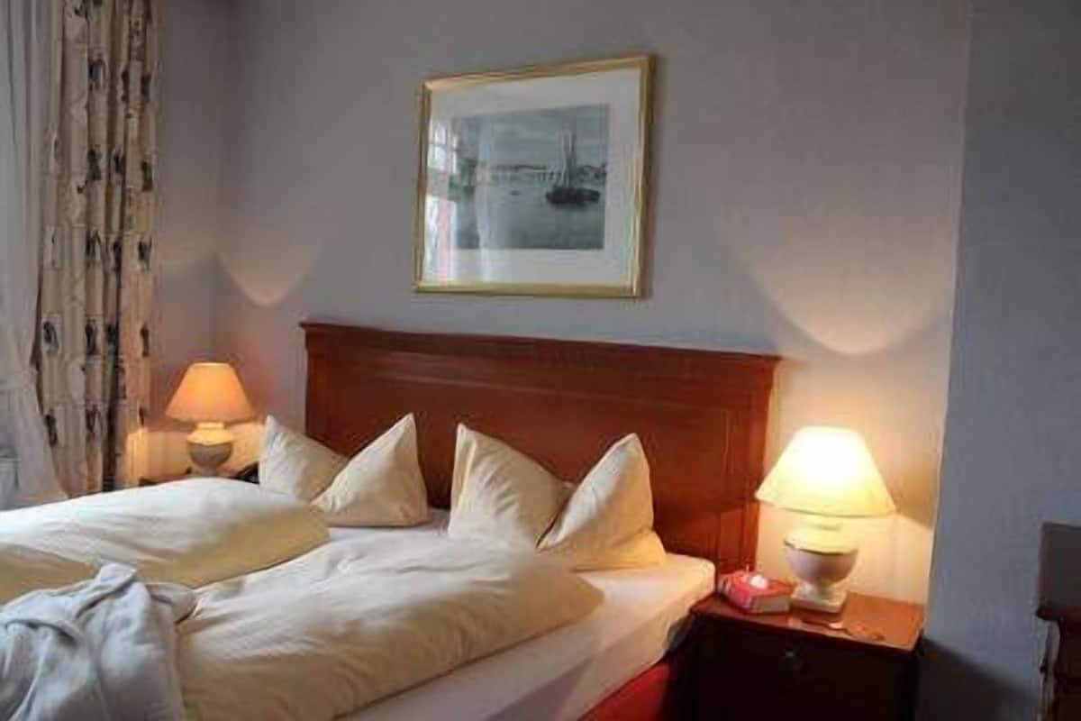 Habitación de hotel con dos camas, cabecero de madera, un cuadro enmarcado en la pared y lámparas de noche.