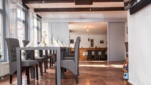 A restaurant with a long dining area, multiple tables, and chairs. There is a counter in the background. - Parkhotel Fischer (Wernigerode)