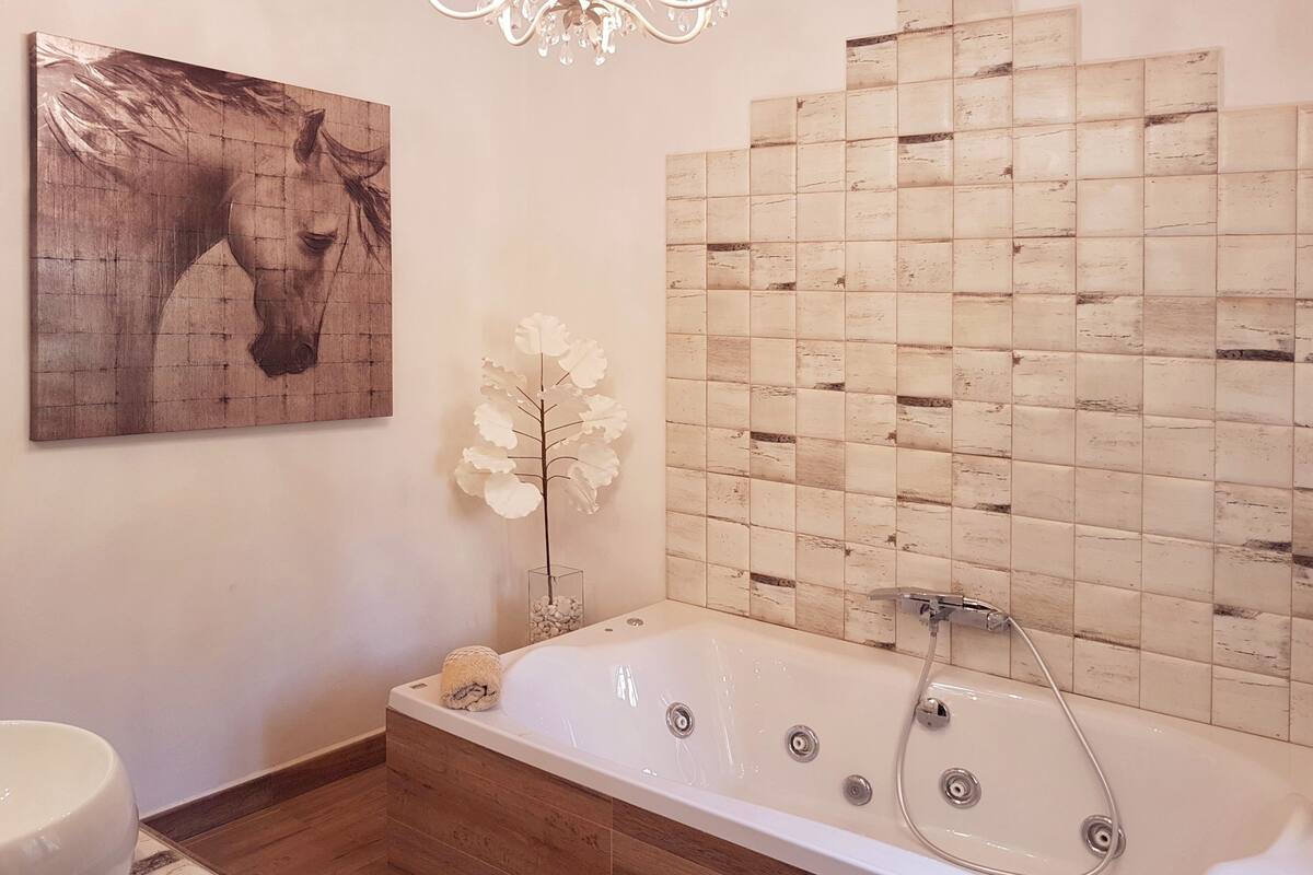 A modern bathroom with a large bathtub, a wooden floor, a white sink, and a decorative horse painting on the wall.