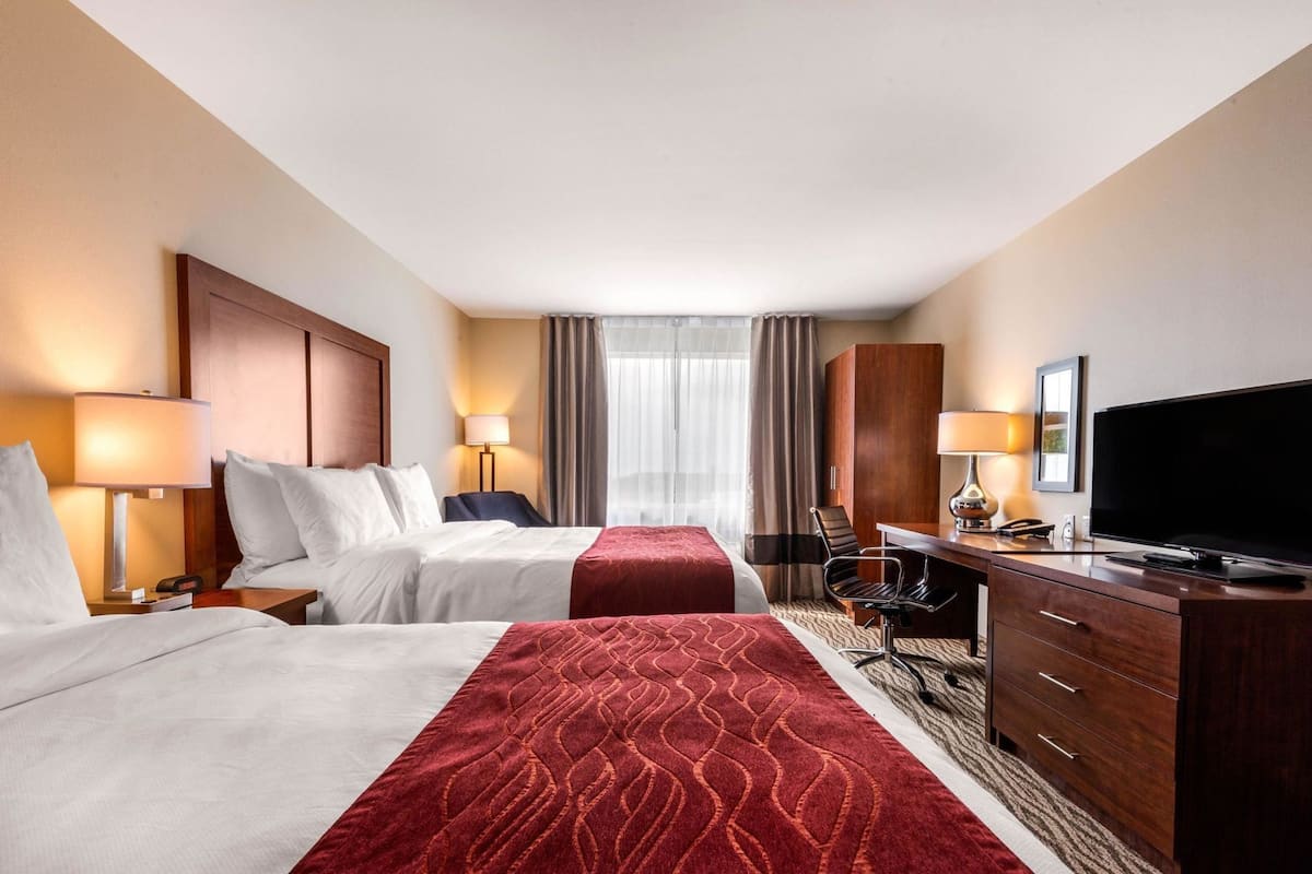 Une chambre d’hôtel avec deux lits, un bureau avec une télévision, une chaise et une armoire.