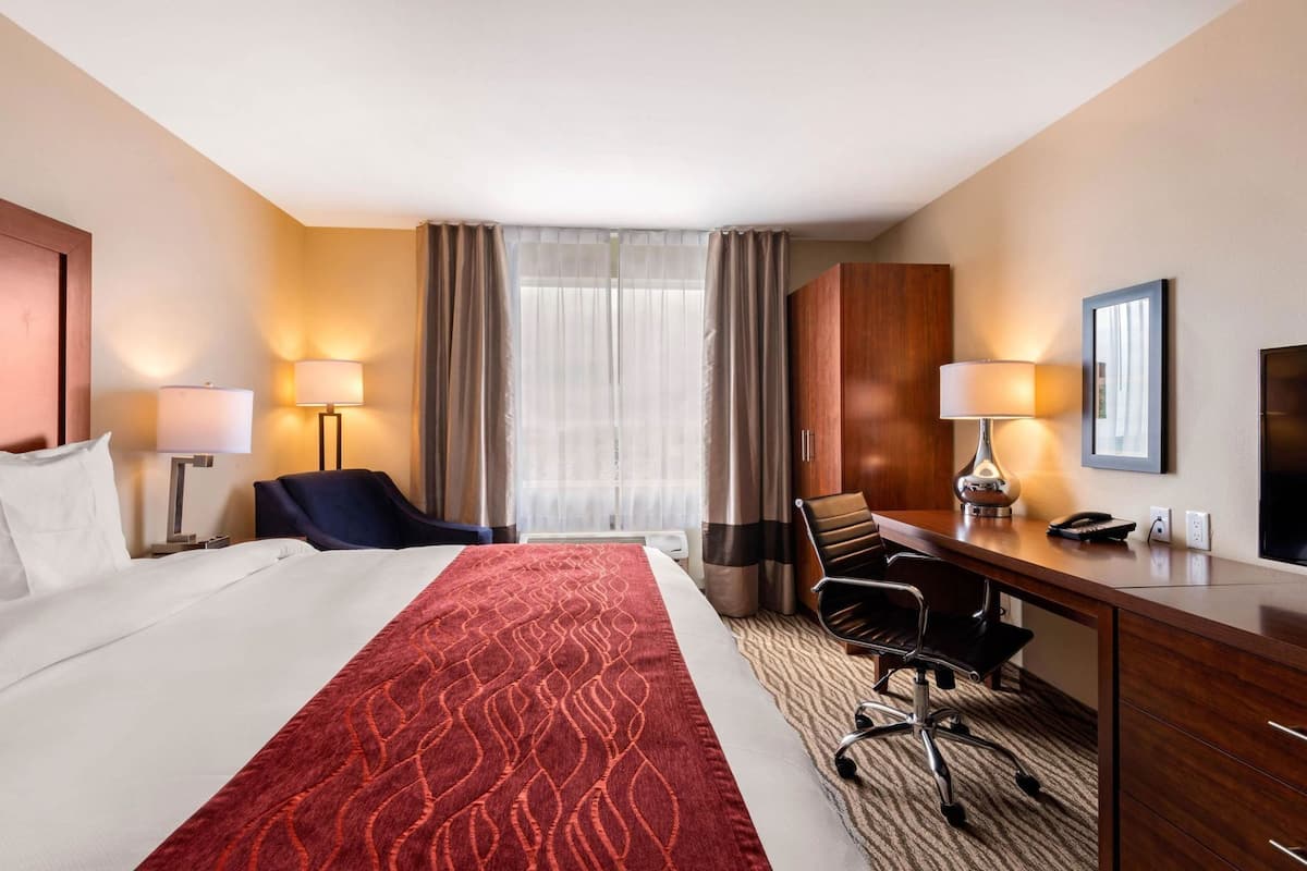 Une chambre d’hôtel avec un grand lit, un bureau avec une chaise, une lampe, un téléphone et un téléviseur.