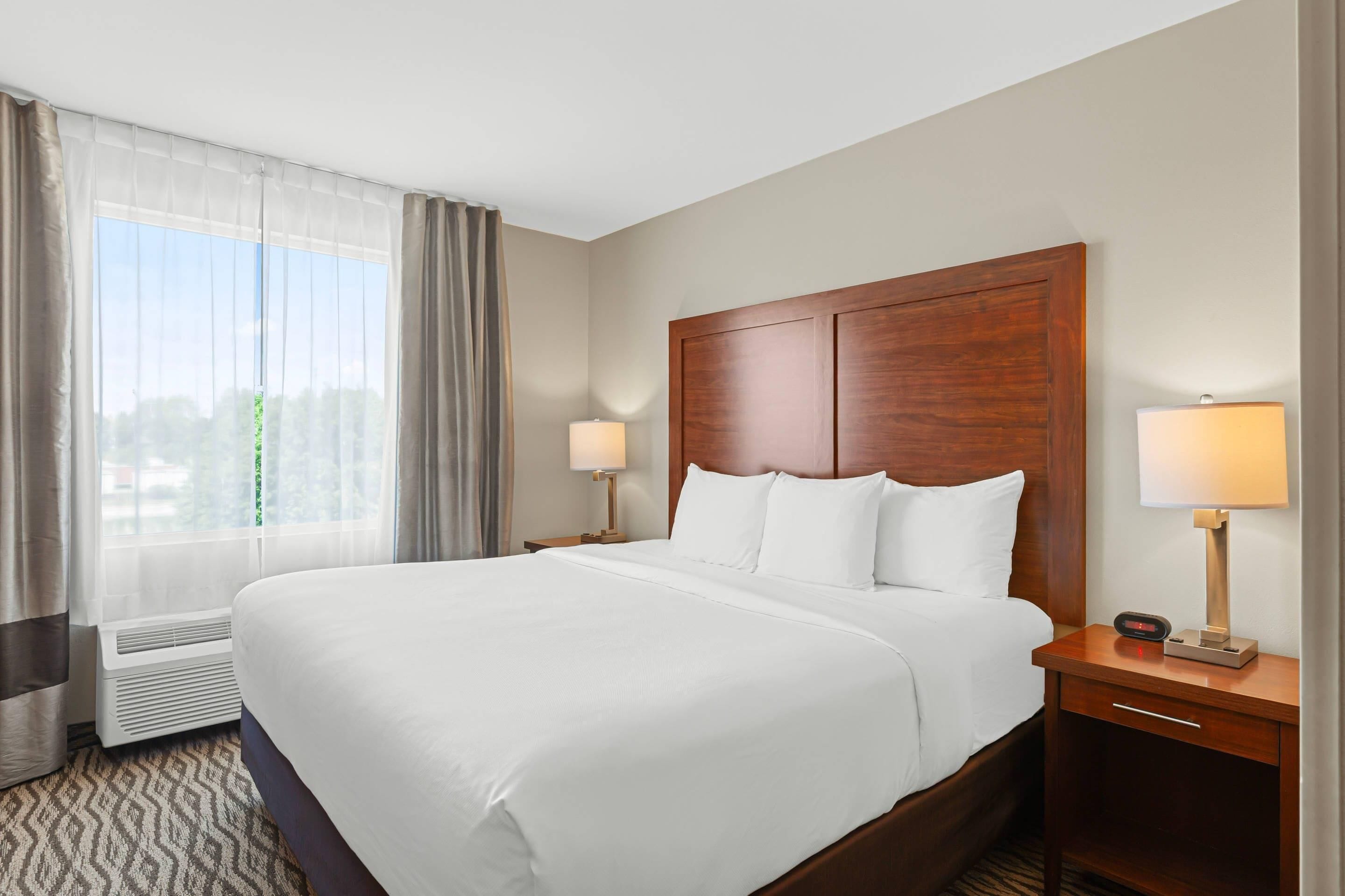 Habitación de hotel con una cama grande, dos lámparas de noche, una mesita y una ventana con cortinas.