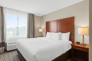 Habitación de hotel con una cama grande, dos lámparas de noche, una mesita y una ventana con cortinas.