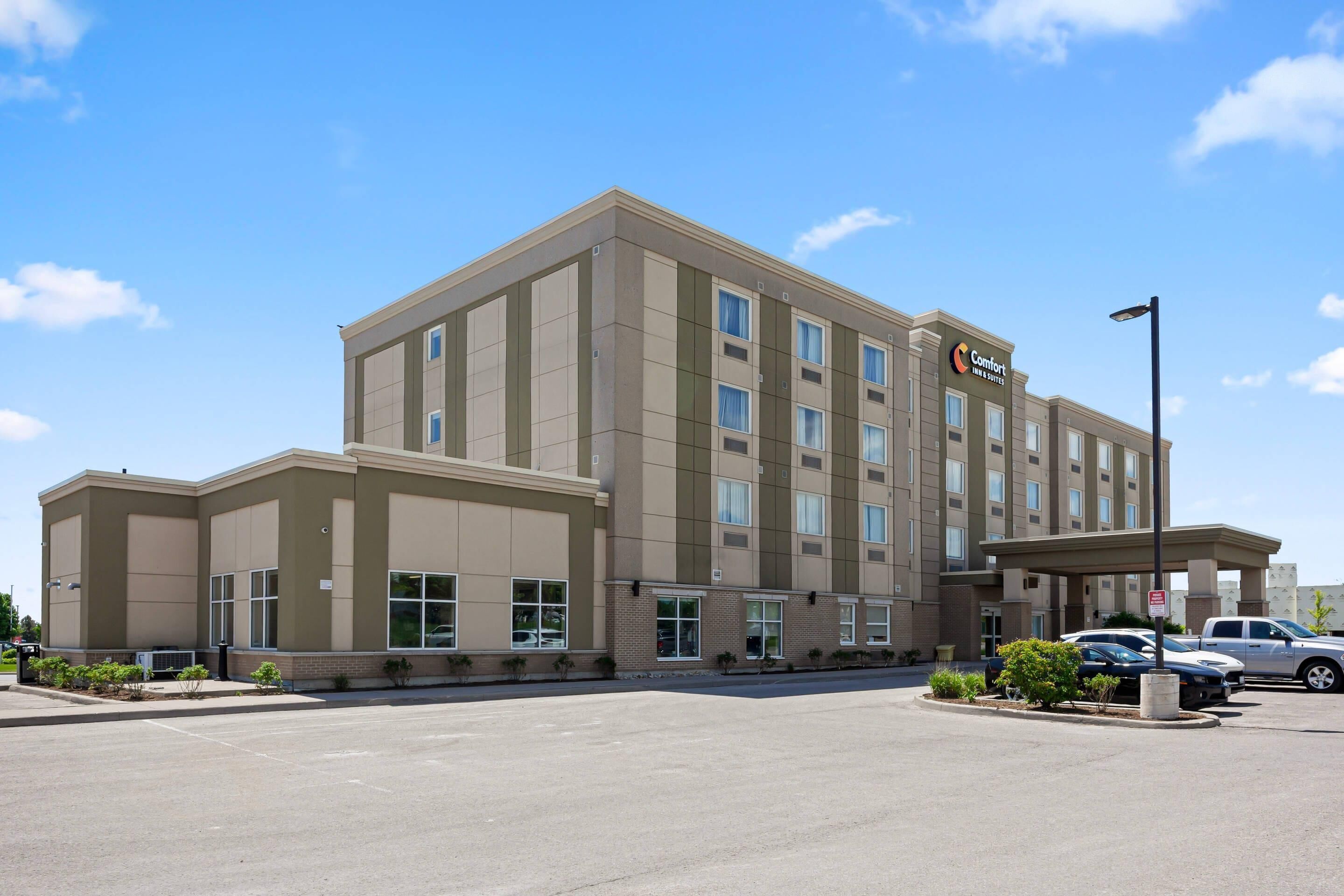 A multi-story hotel with a central entrance, a parking lot, and a clear sky.
