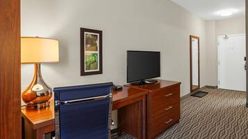 A hotel room with a desk, chair, television, and a door.