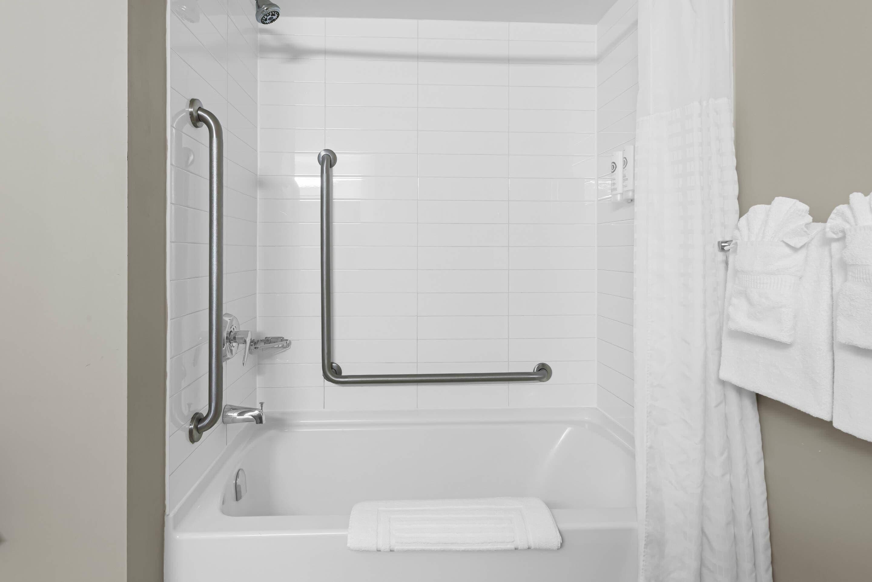 A bathroom with white tiles, a bathtub, a shower area, and a grab bar.
