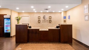 A reception desk with a stone wall backdrop, a sign reading "Comfort Inn & Suites," and a refrigerator stocked with beverages. - Comfort Inn & Suites (Clarington)