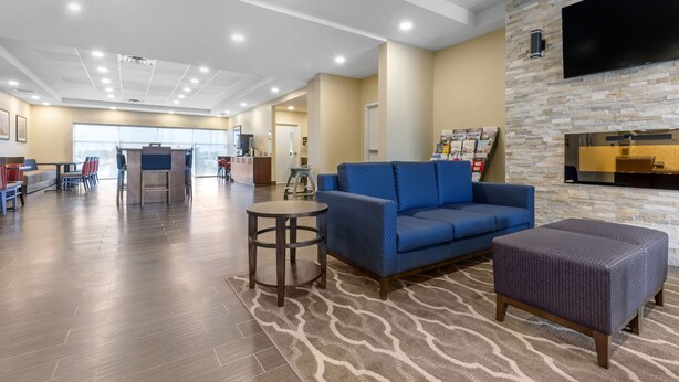 A spacious lobby with a blue sofa, a round table, and a flat-screen TV mounted on a stone wall. - Comfort Inn & Suites (Clarington)