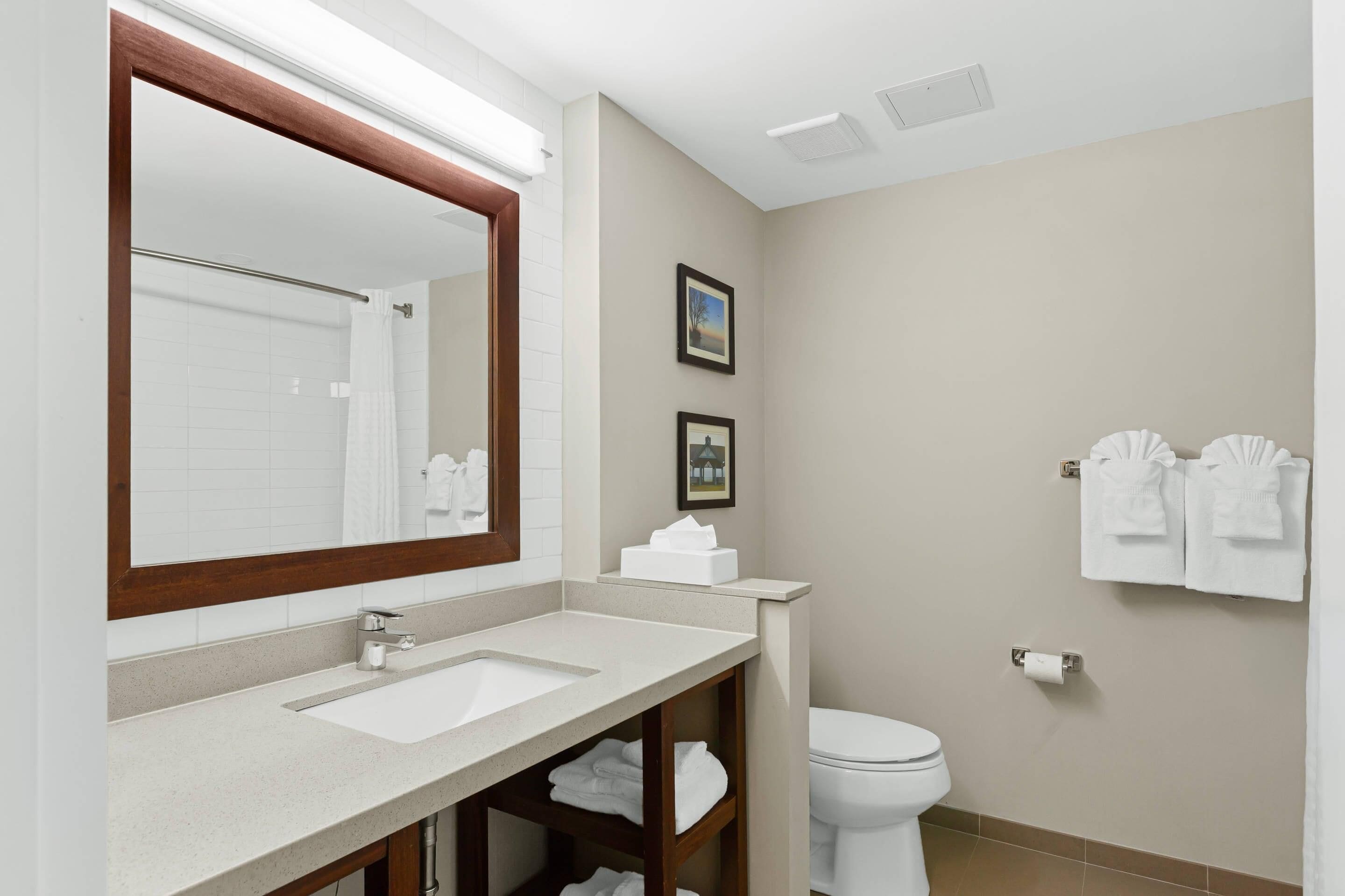 Un baño con un espejo grande, dos lavamanos, un inodoro y toallas colgadas en la pared.
