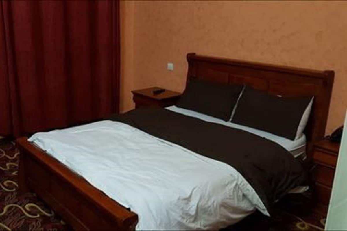 Una cama individual con estructura de madera, una mesita de noche, una cortina roja y una alfombra estampada.