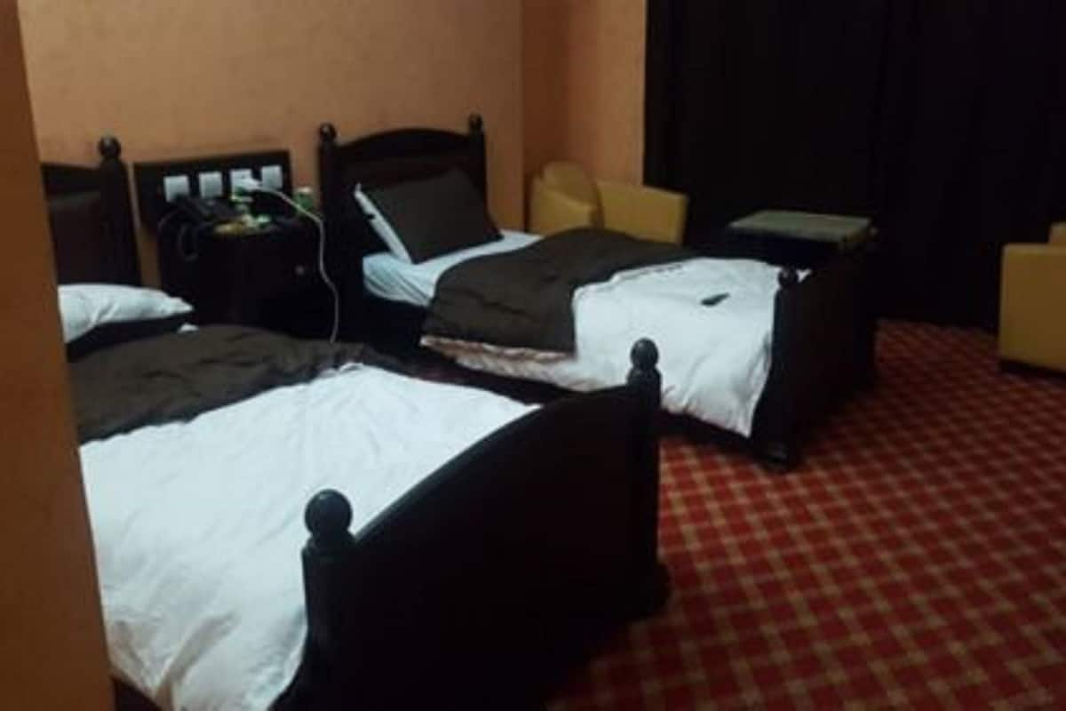 Una habitación de hotel con dos camas, un escritorio, una silla y una alfombra roja a cuadros.