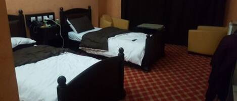 Una habitación de hotel con dos camas, un escritorio, una silla y una alfombra roja a cuadros.