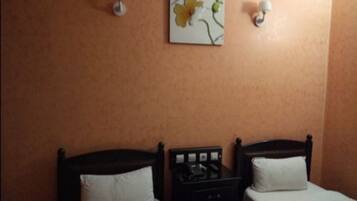 A hotel room with two single beds, a nightstand with a lamp, and a wall-mounted artwork.